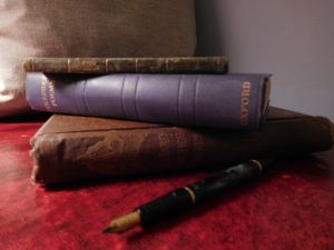 Three old volumes of poetry on a red leather desk with a fountain pen in the foreground