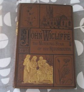 A photograph of a Victorian book with decorative cloth binding entitled John Wicliffe.